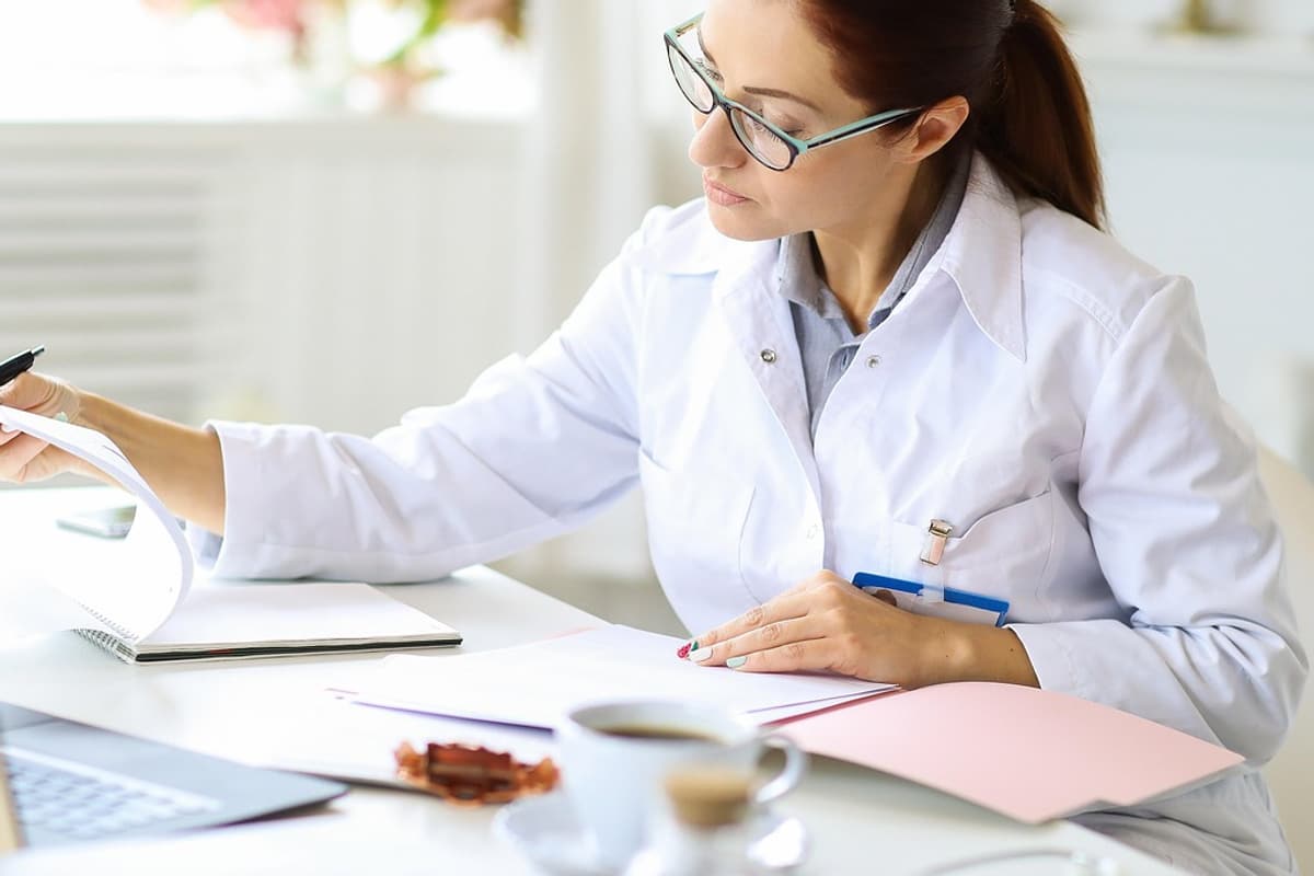 A clinician at a desk turning the pages of a printed document.