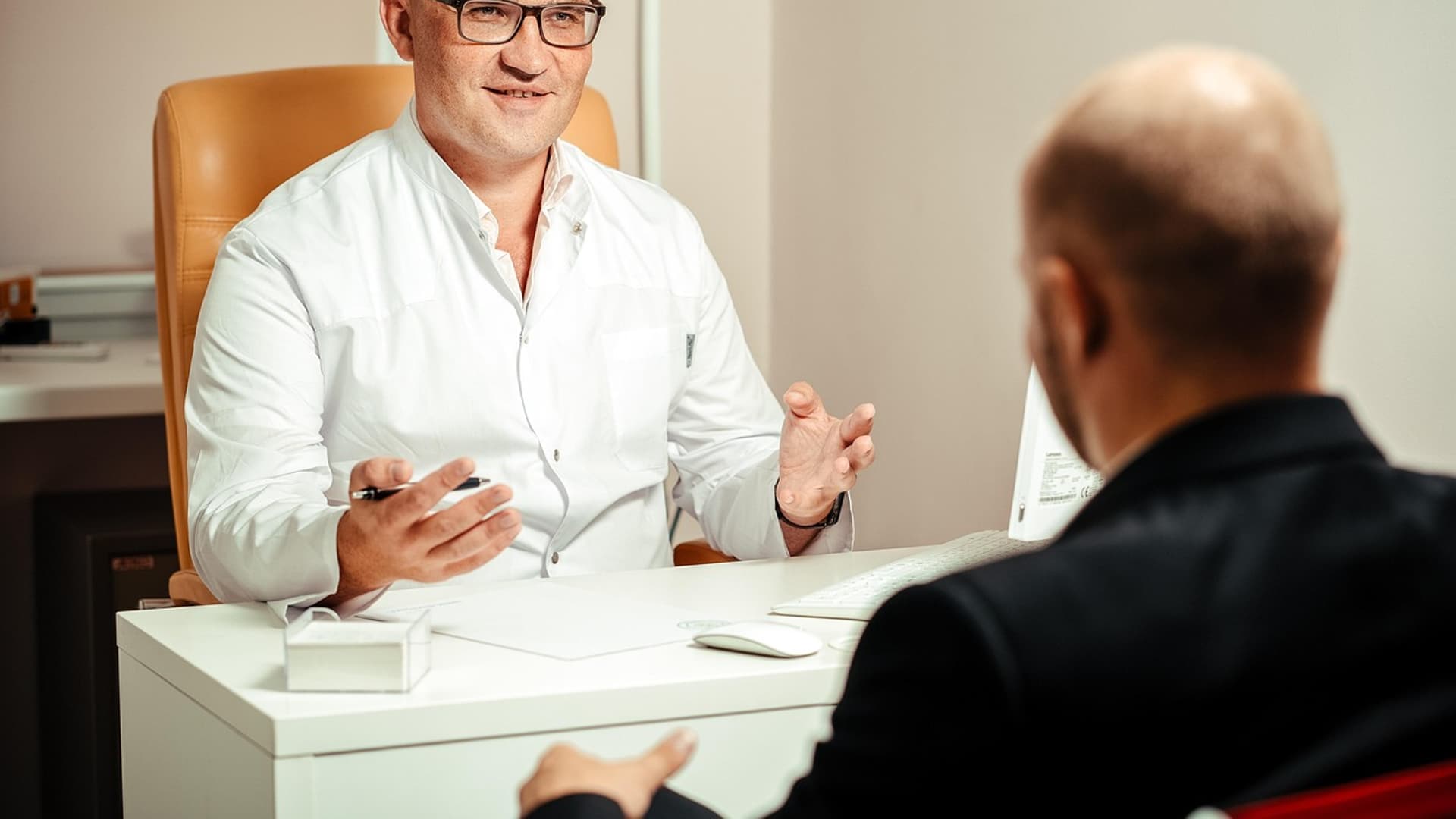 A doctor talking with a patient across a desk in a consulting room.